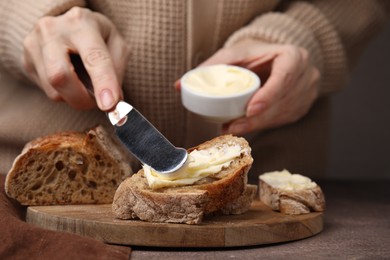 Photo of Woman spreading butter onto bread at wooden table, closeup