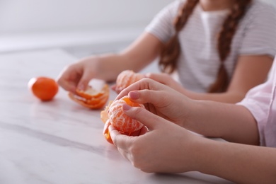 Photo of Girls peeling fresh tangerines at table in kitchen, closeup