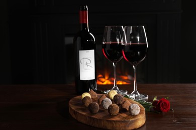 Photo of Red wine, chocolate truffles and rose flower on wooden table against fireplace