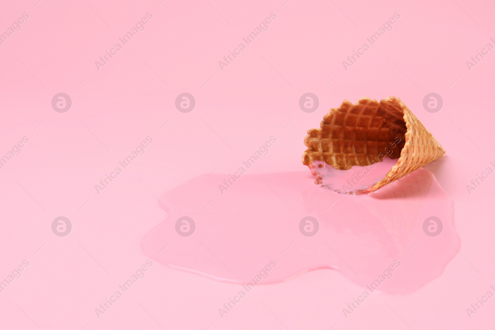 Photo of Melted ice cream and wafer cone on pink background, closeup. Space for text