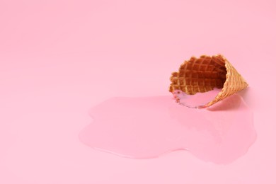Melted ice cream and wafer cone on pink background, closeup. Space for text