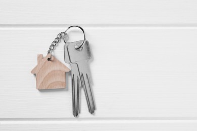 Photo of Key with keychain in shape of house on white wooden table, top view. Space for text
