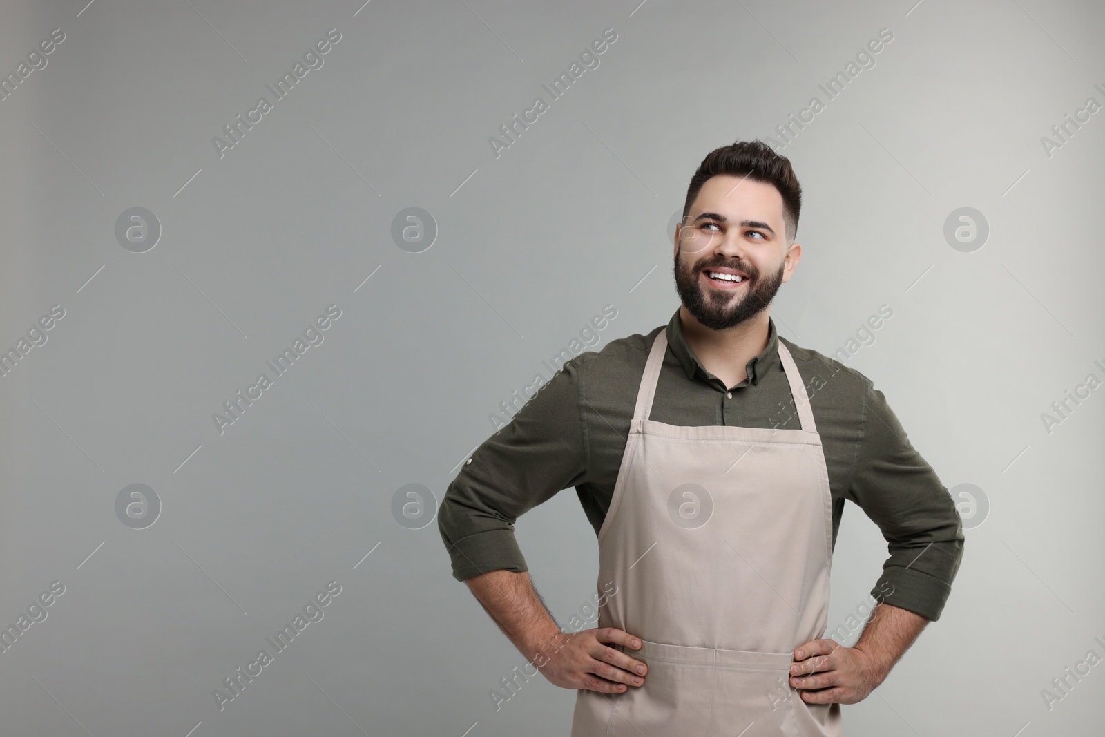 Photo of Smiling man in kitchen apron on grey background. Mockup for design