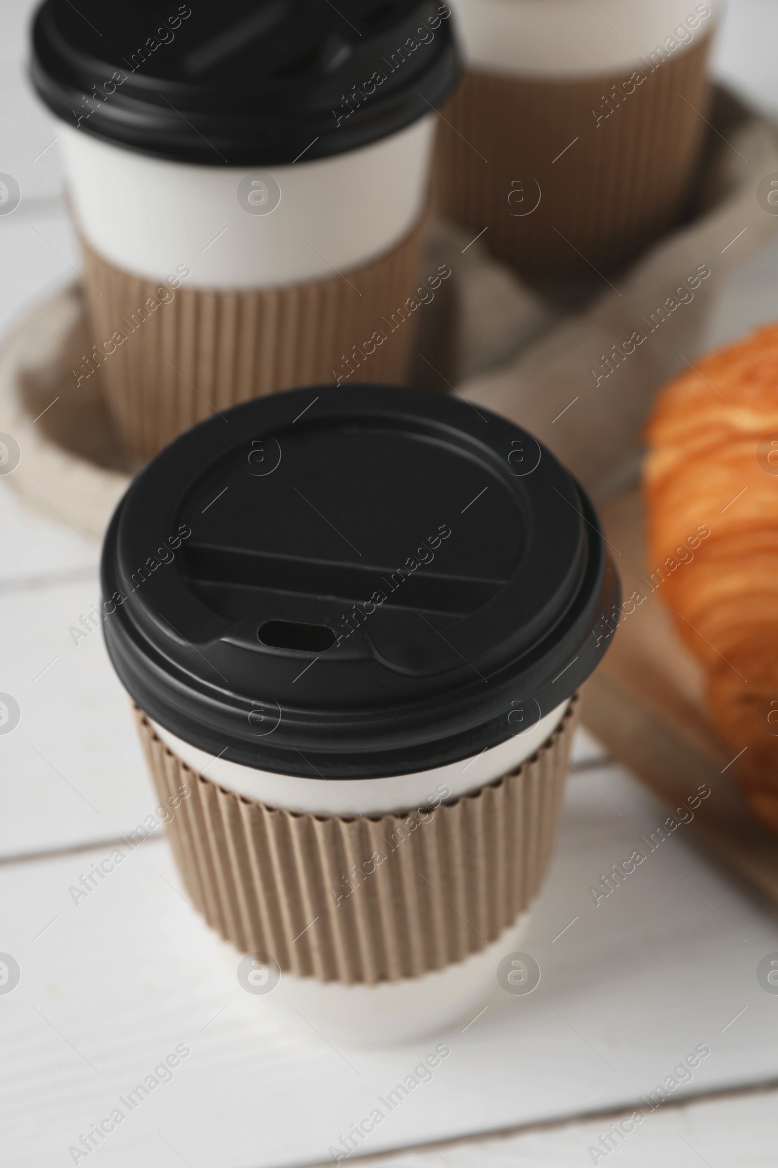 Photo of Coffee to go. Paper cups with tasty drink and croissant on white table, closeup