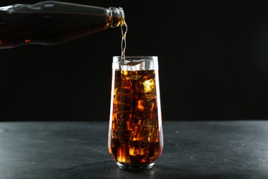 Photo of Pouring refreshing soda water from bottle into glass on black table