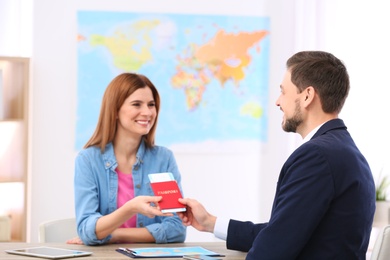 Photo of Male manager giving passport with ticket to client in travel agency