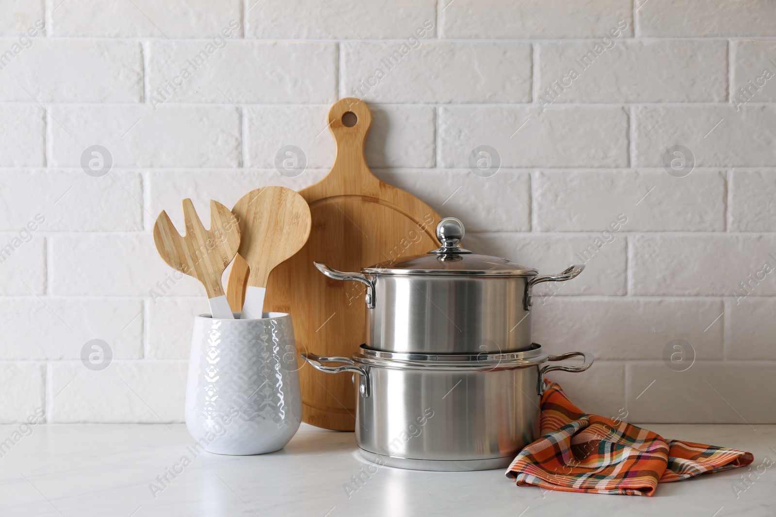 Photo of Pots and kitchen utensils on table near white brick wall