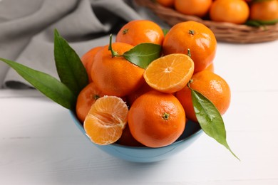 Photo of Fresh ripe juicy tangerines and green leaves in bowl on white wooden table, closeup