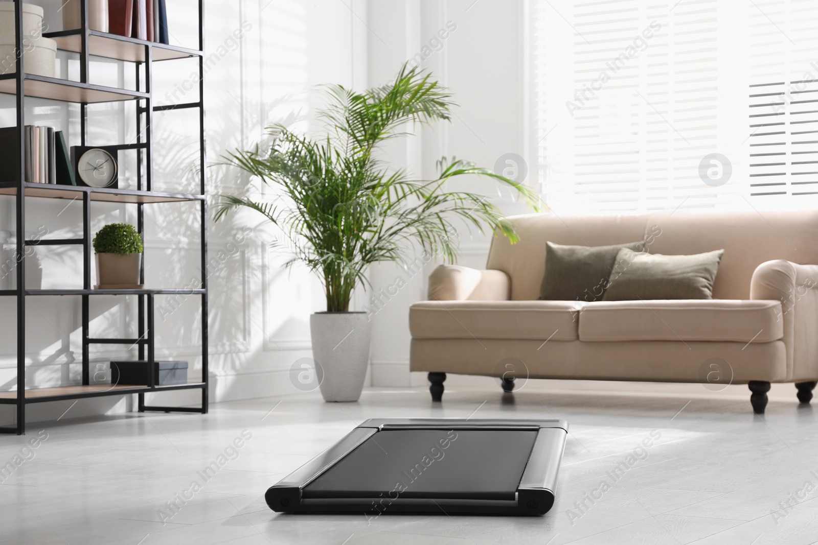 Photo of Modern walking treadmill in living room. Home gym equipment