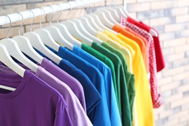 Photo of Rack with rainbow clothes on brick wall background