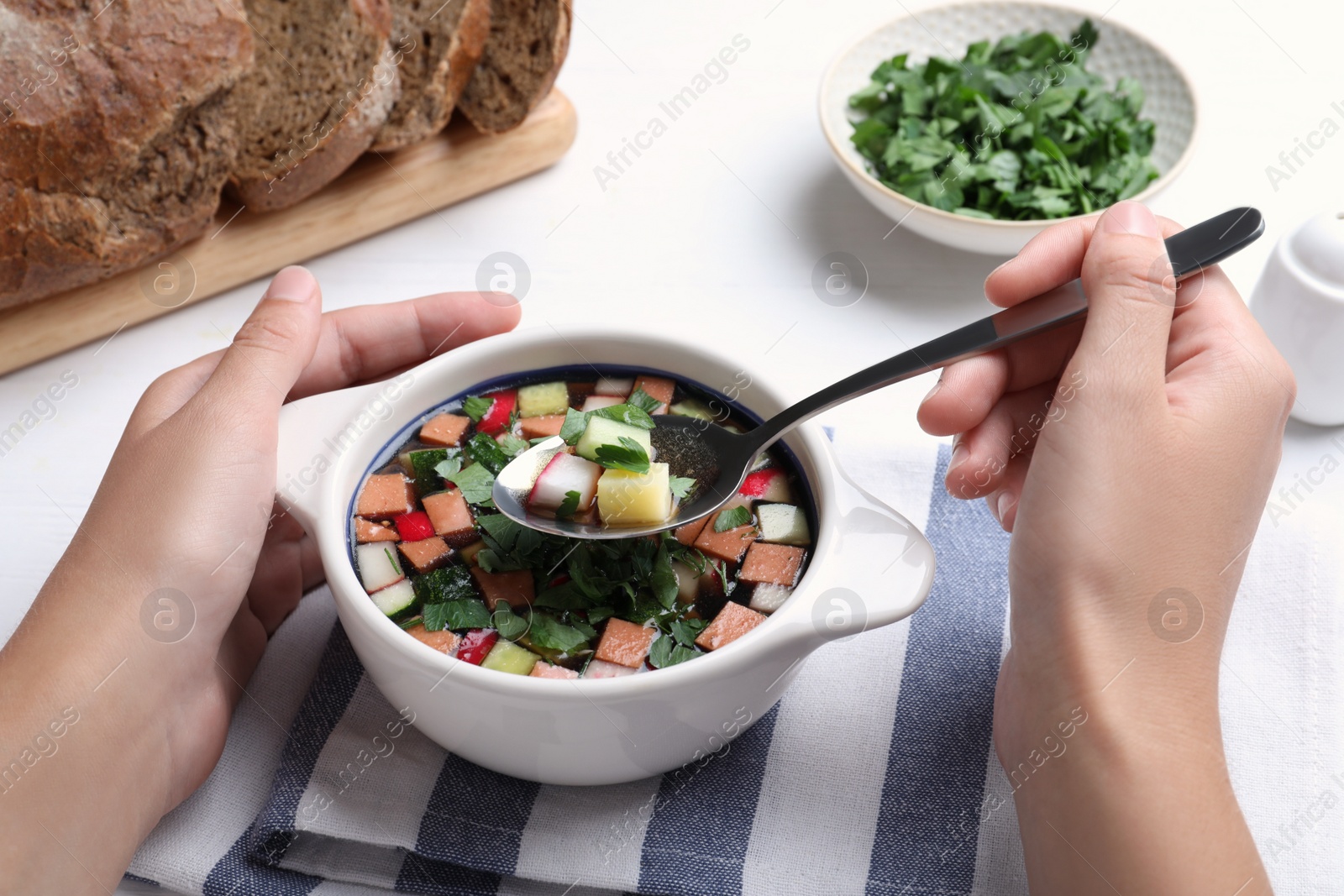 Photo of Woman eating delicious cold okroshka with kvass at white wooden table, closeup. Traditional Russian summer soup