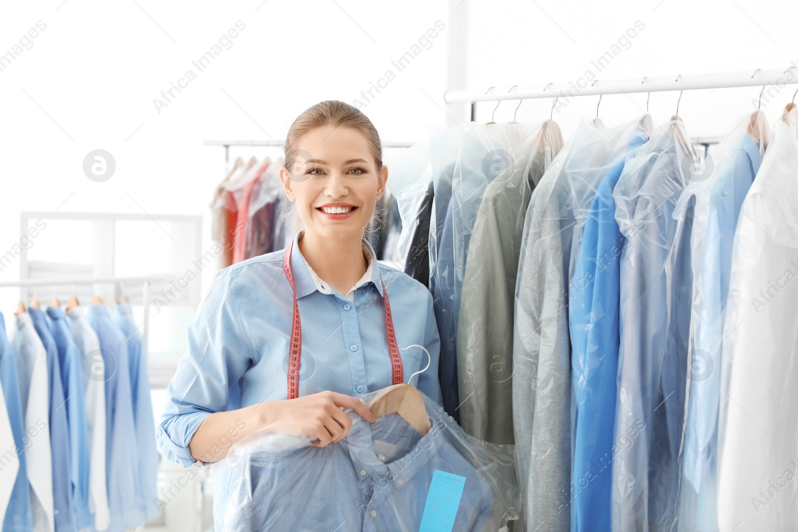 Photo of Young woman holding hanger with shirt in plastic bag at dry-cleaner's