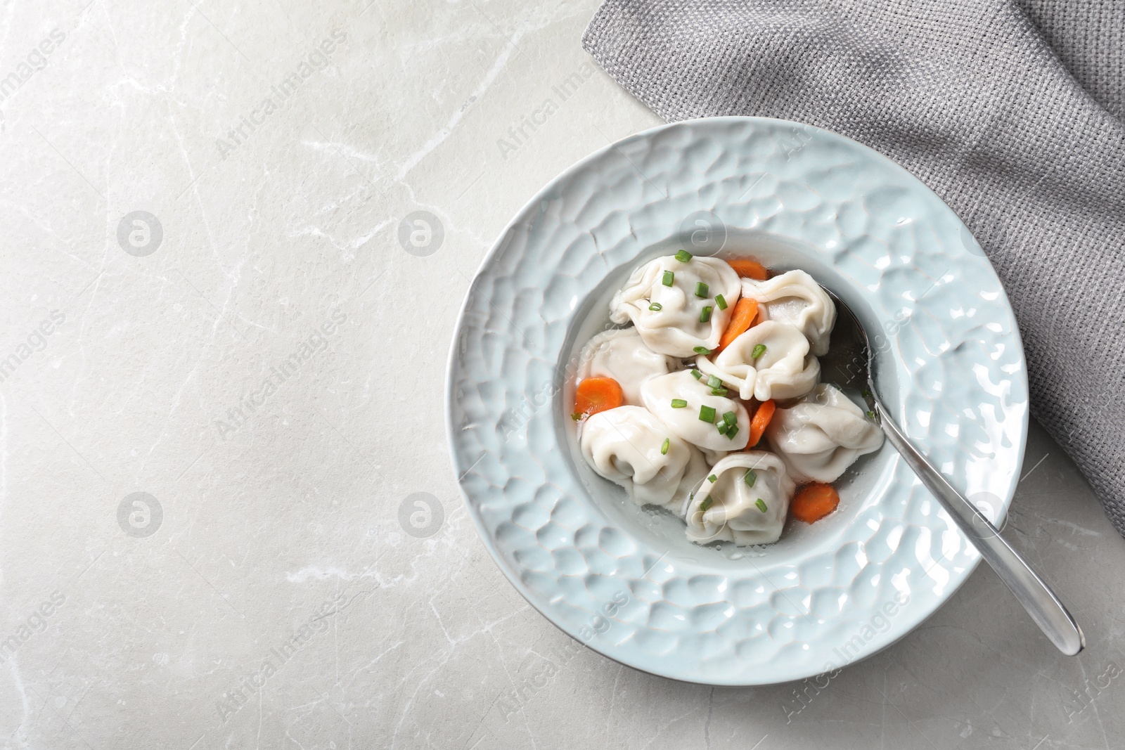 Photo of Plate of tasty dumplings in broth with spoon on grey marble table, top view. Space for text