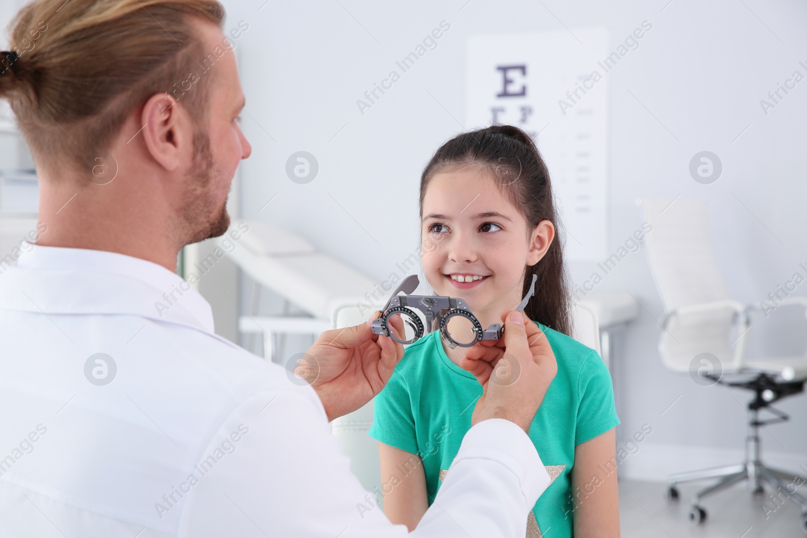 Photo of Children's doctor putting trial frame on little girl in clinic. Eye examination