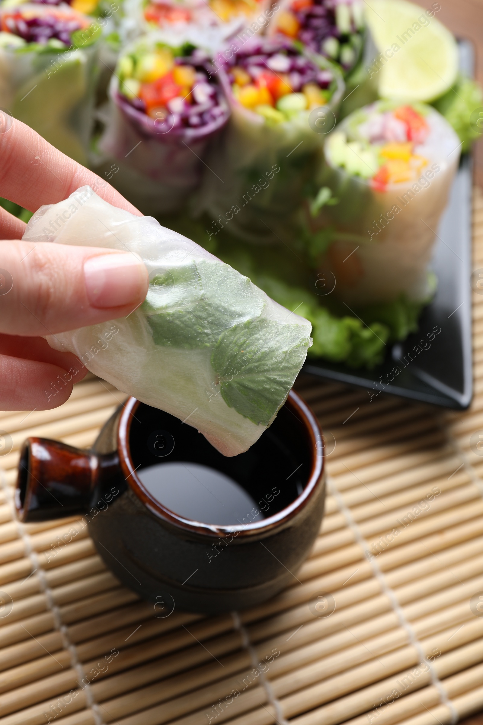 Photo of Woman dipping delicious spring roll into soy sauce at table, closeup