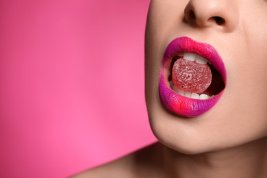 Photo of Young woman with beautiful makeup holding candy in lips on pink background, closeup. Space for text