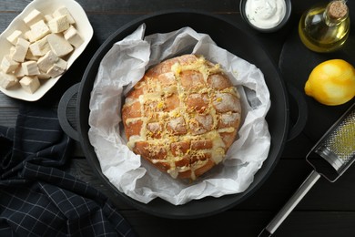 Photo of Freshly baked bread with tofu cheese and lemon zest served on black wooden table, flat lay