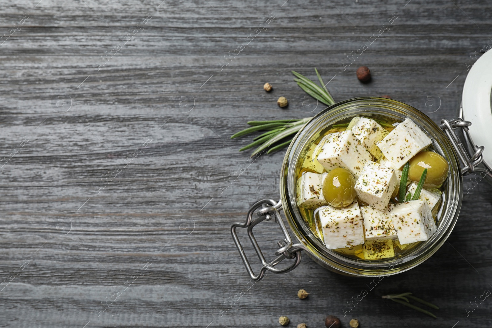 Photo of Pickled feta cheese in jar on grey wooden table, top view. Space for text