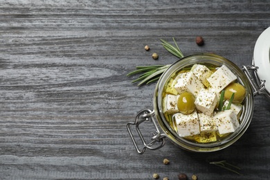 Photo of Pickled feta cheese in jar on grey wooden table, top view. Space for text