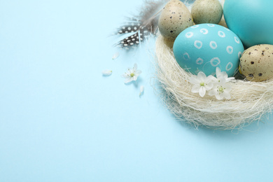 Photo of Colorful Easter eggs in decorative nest on light blue background. Space for text