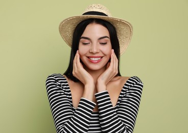 Beautiful young woman with straw hat on light green background