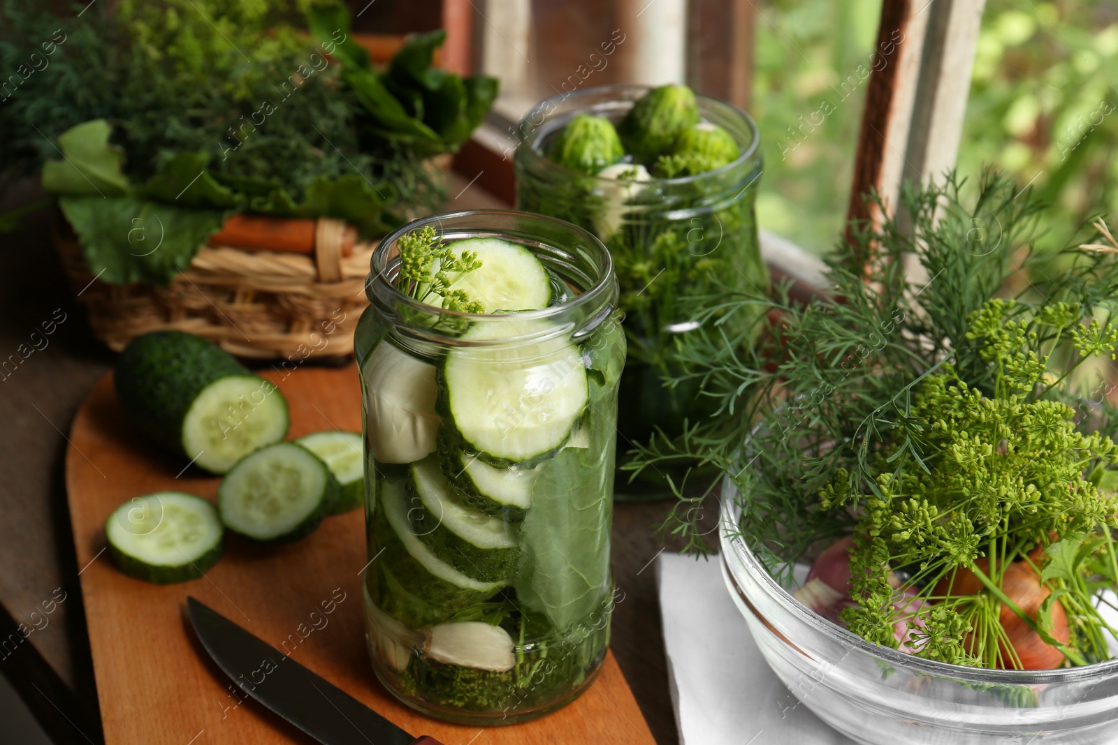 Photo of Glass jars, fresh cucumbers and herbs on wooden table indoors. Pickling recipe