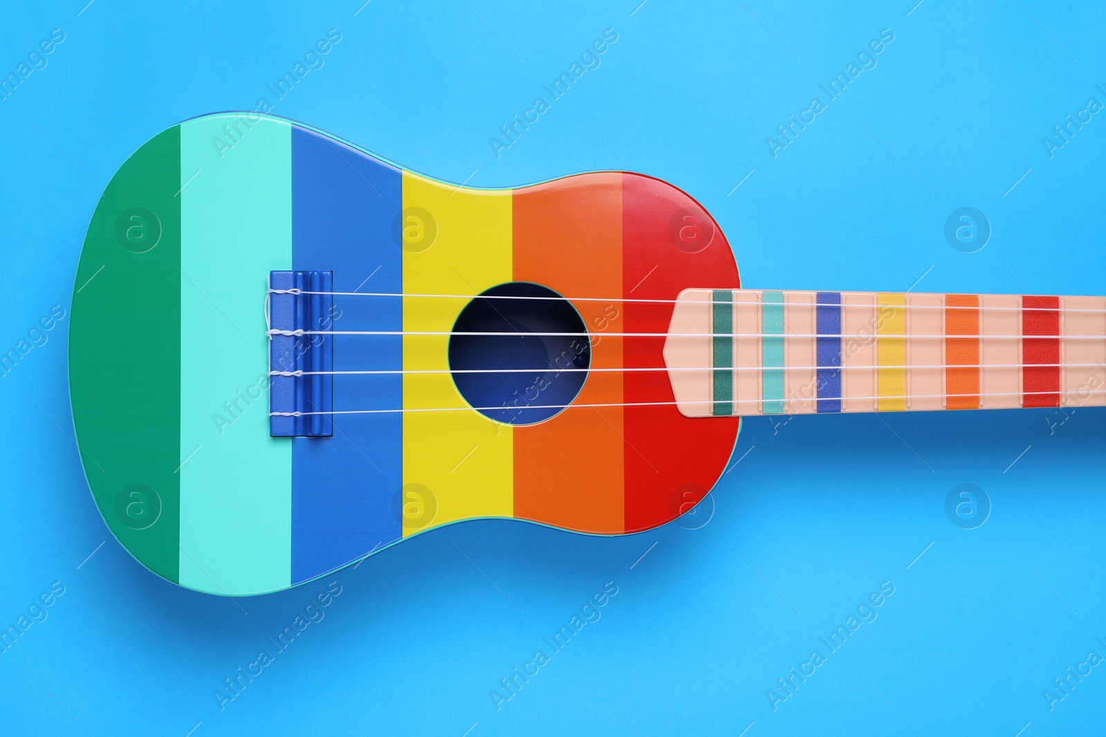 Photo of Colorful ukulele on light blue background, top view. String musical instrument