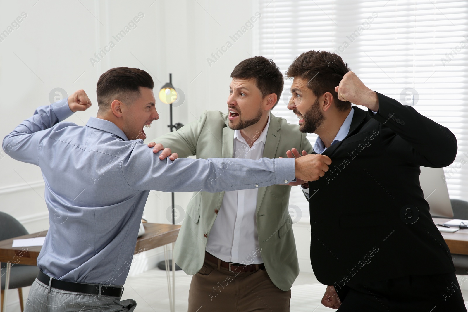 Photo of Man interrupting colleagues fight at work in office