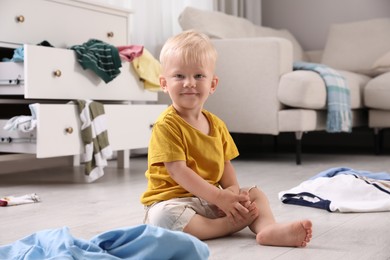 Photo of Cute little boy sitting on floor in messy room