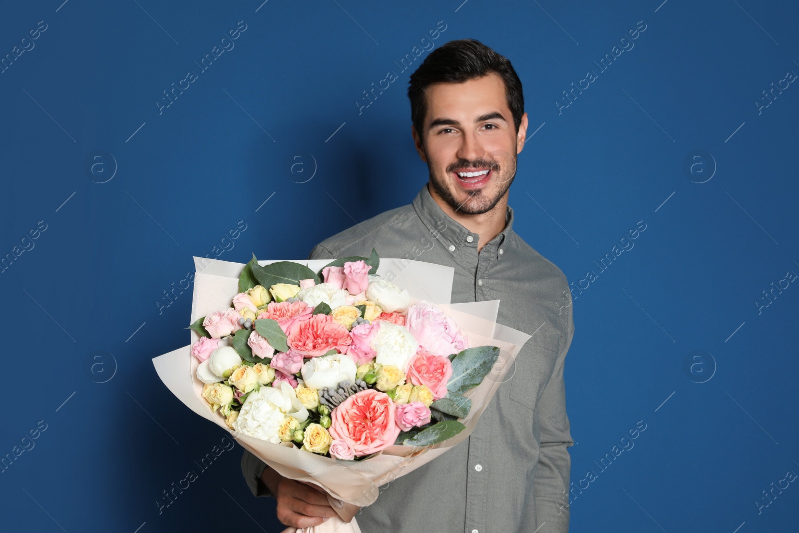 Photo of Young handsome man with beautiful flower bouquet on blue background