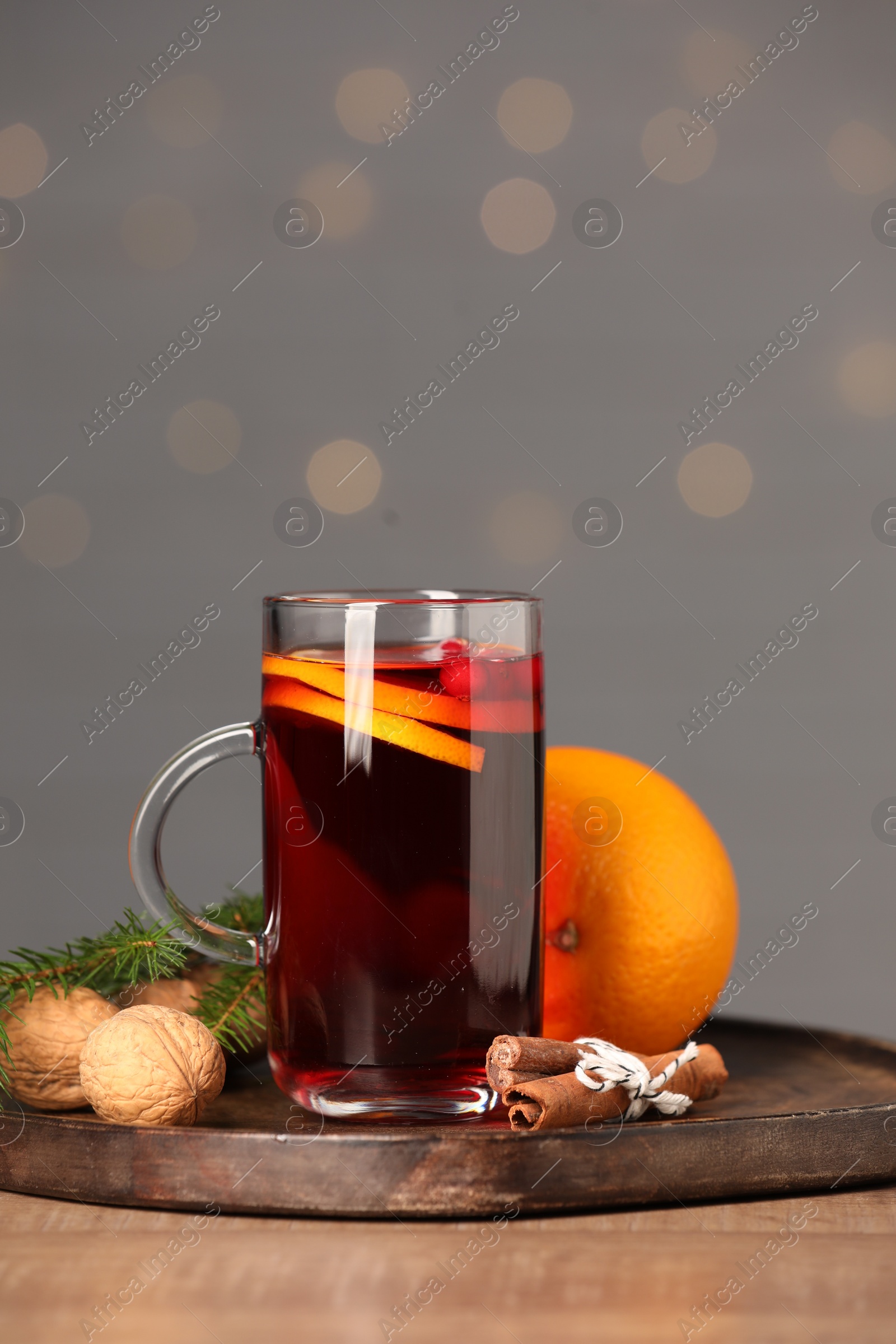 Photo of Aromatic mulled wine in glass cup on wooden table against grey background with blurred lights