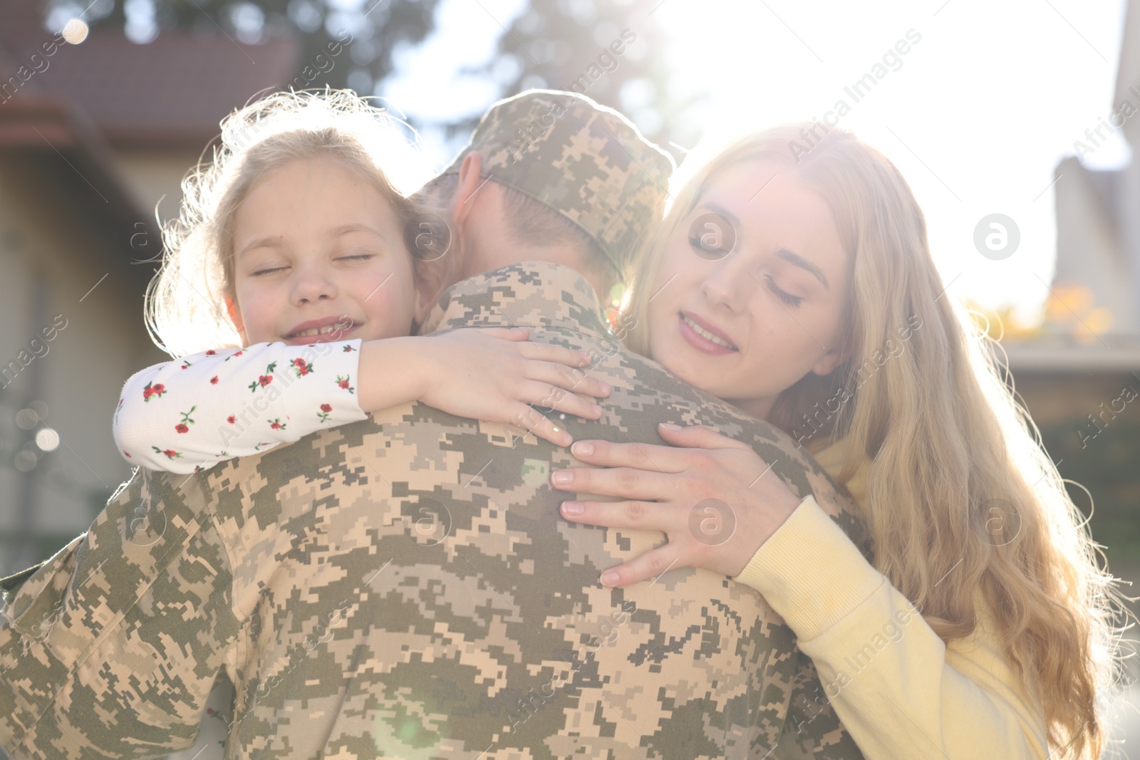 Photo of Daughter and wife hugging soldier in Ukrainian military uniform outdoors. Family reunion