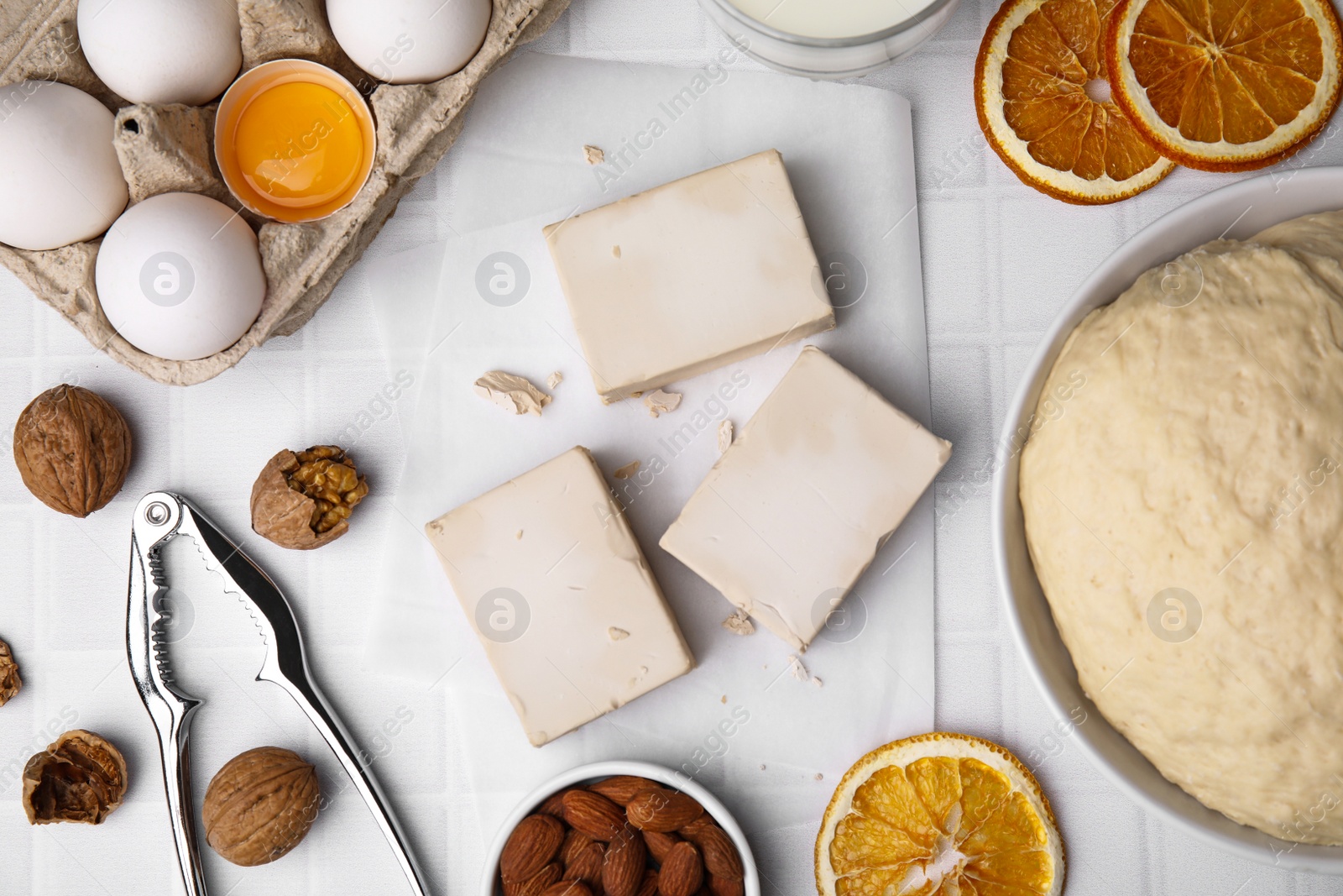 Photo of Yeast and ingredients for dough on white tiled table, flat lay