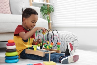 Cute African-American boy playing with colorful toys on floor at home