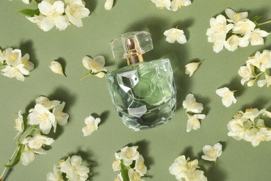 Photo of Aromatic perfume in bottle among beautiful jasmine flowers on pale green background, flat lay