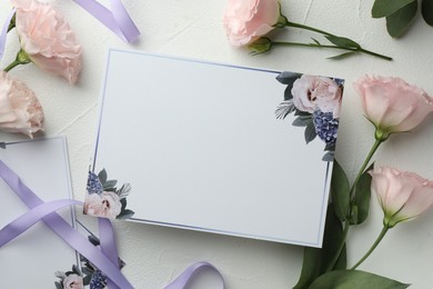 Photo of Blank invitation card, ribbon and pink flowers on white table, flat lay