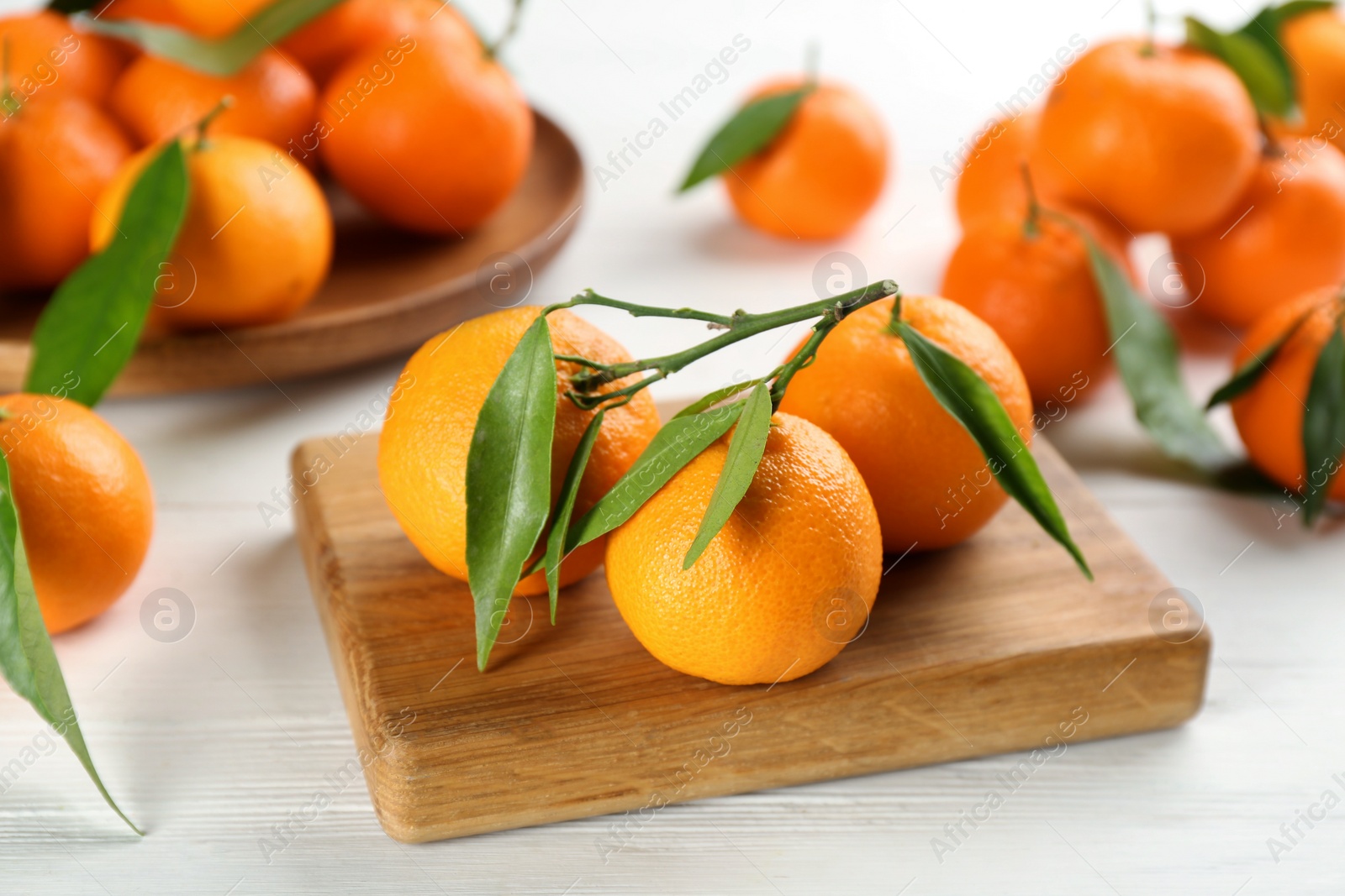 Photo of Fresh ripe tangerines with green leaves on white wooden table