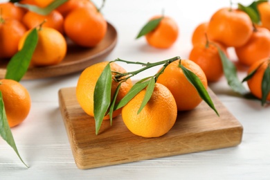 Photo of Fresh ripe tangerines with green leaves on white wooden table