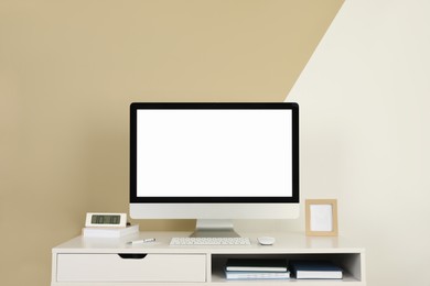 Photo of Modern computer, digital clock and office supplies on white wooden table near color wall