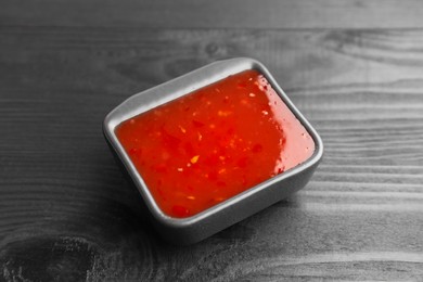 Photo of Spicy chili sauce in bowl on black wooden table, closeup