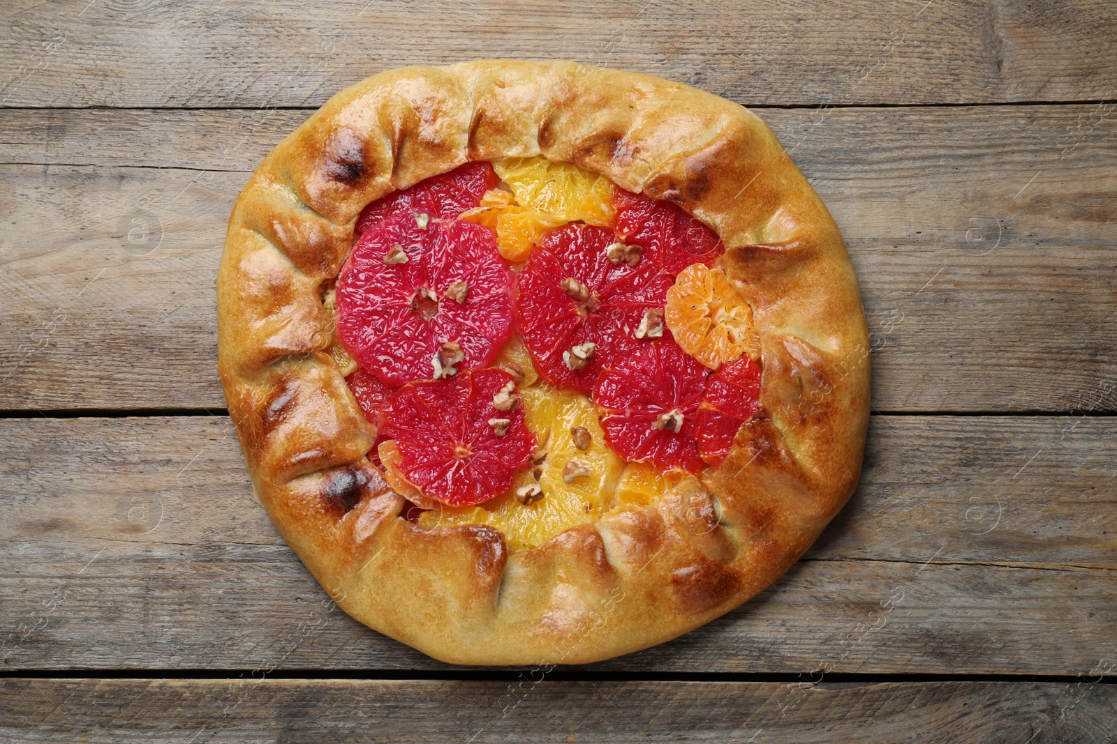 Photo of Delicious galette with citrus fruits and walnuts on wooden table, top view