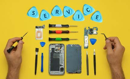 Image of Man repairing broken smartphone on yellow background, top view