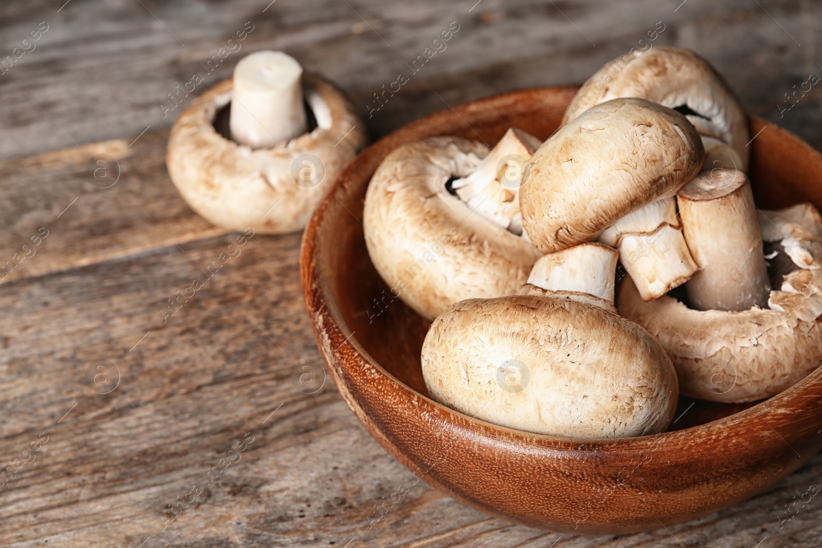 Photo of Bowl of fresh champignon mushrooms on wooden table, closeup. Space for text