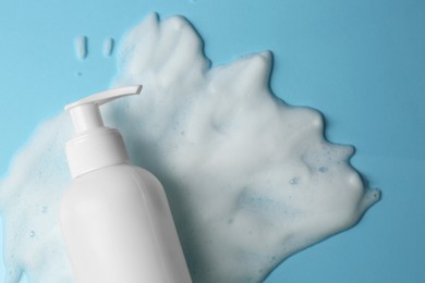 Photo of Bottle of face cleanser and white foam on light blue background, top view with space for text. Skin care cosmetic