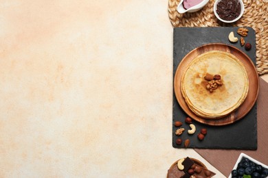 Photo of Delicious crepes with nuts, blueberries, chocolate and jam on beige table, flat lay. Space for text