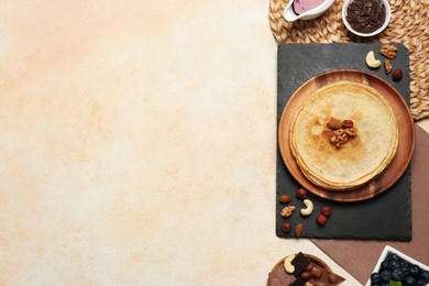 Delicious crepes with nuts, blueberries, chocolate and jam on beige table, flat lay. Space for text