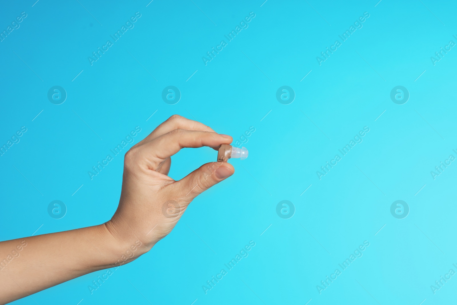 Photo of Female doctor holding hearing aid on color background, closeup view with space for text. Medical object