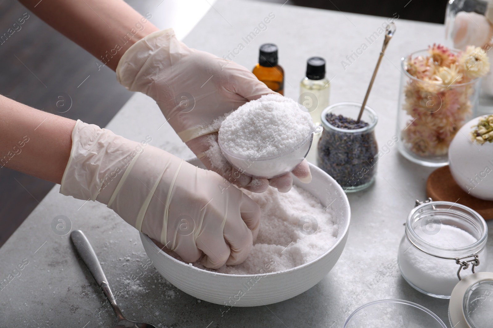 Photo of Woman in gloves making bath bomb at grey table, closeup