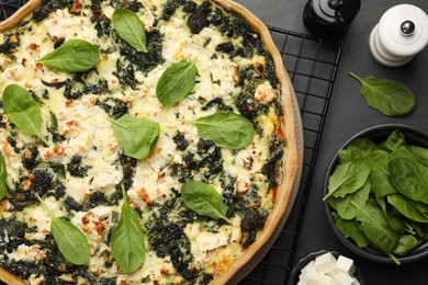 Photo of Delicious homemade spinach quiche and ingredients on black table, flat lay