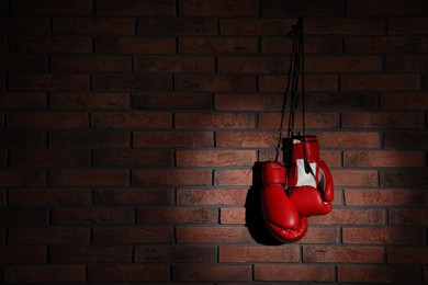Photo of Pair of red boxing gloves hanging in spotlight on brick wall, space for text